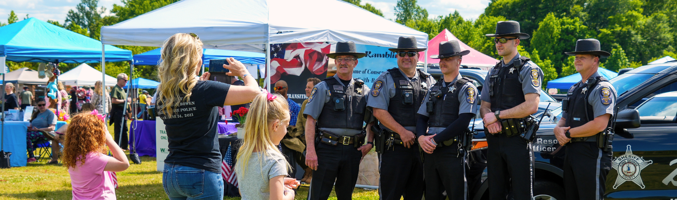 Family taking a photo of the sheriff and deputies lined up in front of the D.A.R.E. SUV