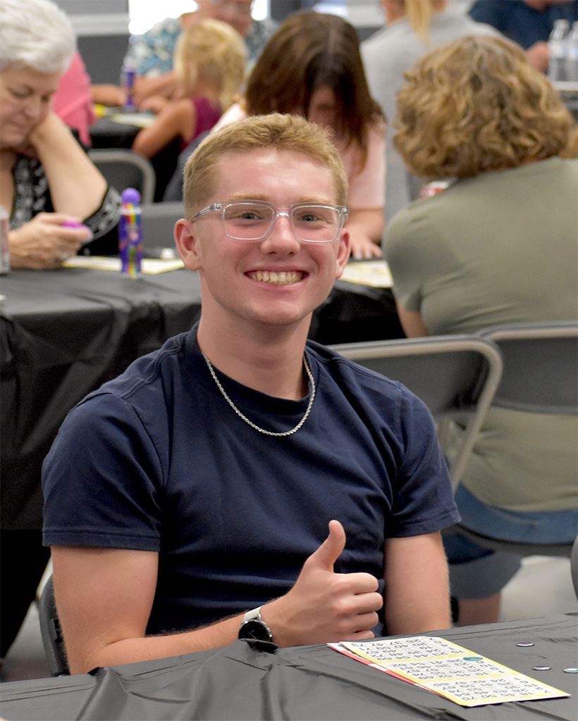 A man is giving a thumbs up in front of his bingo card.